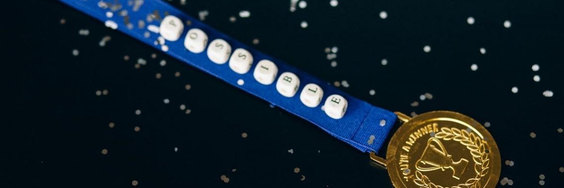 Close-up of a gold medal on a blue ribbon with 'possible' beading, symbolizing achievement.